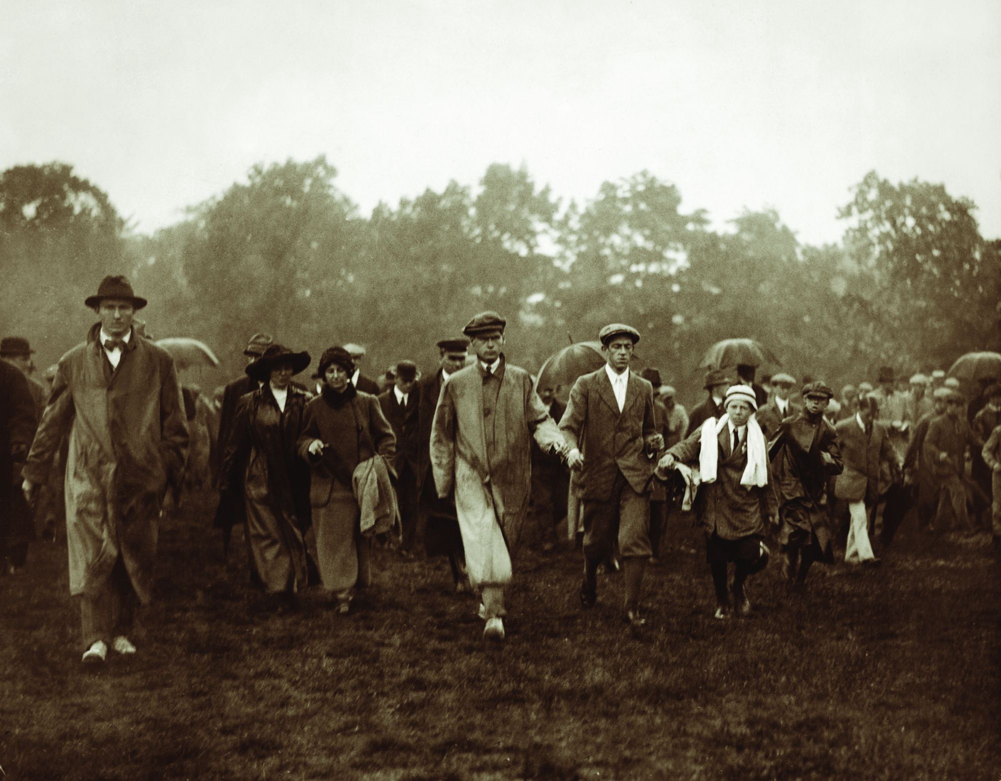 Historic photograph of golfers and spectators walking the course in the rain